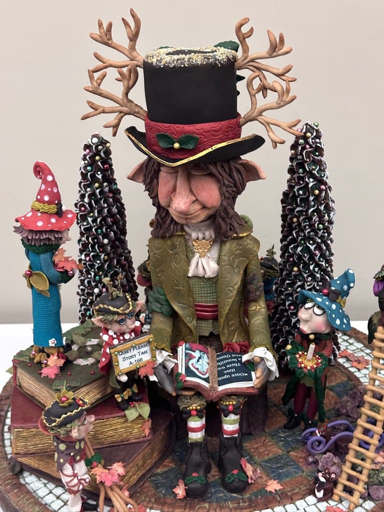 A gingerbread competition entry of an enchanted-forest storyteller with elves